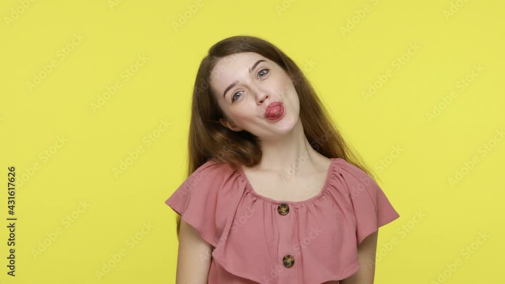 Portrait of childish woman with disobedient behavior, having brown hair in elegant dress sticking out tongue at camera, teasing with happy foolish expression. Indoor shot isolated on yellow background Portrait of childish woman with disobedient behavior, having brown hair in elegant dress sticking out tongue at camera, teasing with happy foolish expression. Indoor shot isolated on yellow background