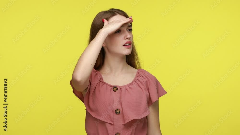 Focused woman with brown hair in dress looking far away with hand over head, expecting to see something at horizon, searching on distance. Indoor studio shot isolated on yellow background. Focused woman with brown hair in dress looking far away with hand over head, expecting to see something at horizon, searching on distance. Indoor studio shot isolated on yellow background.