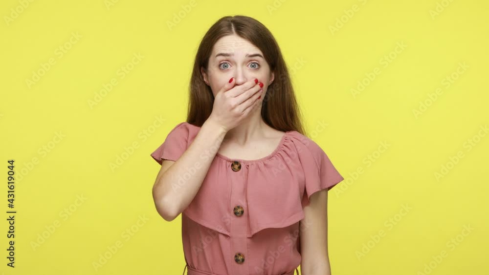 Terrified woman with big eyes covering her mouth to keep silence, surprised by horrible truth, holding breath and promising don't tell secret. Indoor studio shot isolated on yellow background. Terrified woman with big eyes covering her mouth to keep silence, surprised by horrible truth, holding breath and promising don't tell secret. Indoor studio shot isolated on yellow background.