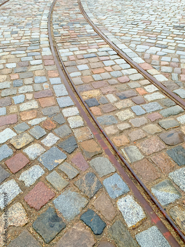 Old tram rails on paving stones converging towards the horizon, selective focus