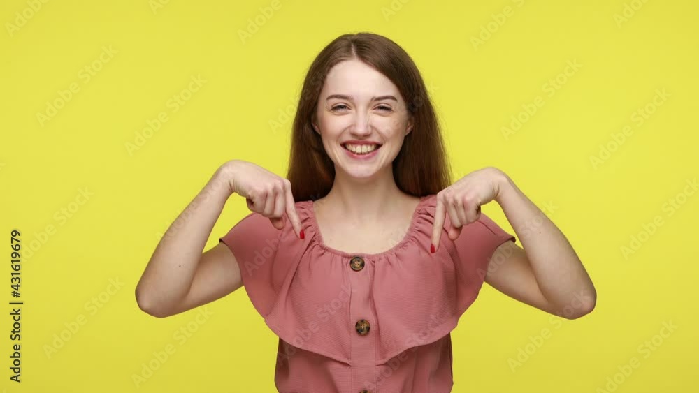 Smiling positive woman in summer dress pointing fingers down showing thumbs up, asking to subscribe and like her post, happily looking at camera. Indoor studio shot isolated on yellow background. Smiling positive woman in summer dress pointing fingers down showing thumbs up, asking to subscribe and like her post, happily looking at camera. Indoor studio shot isolated on yellow background.