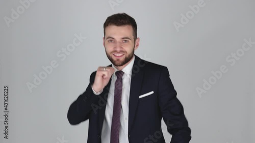 Young Handsome Businessman in suit tired but dancing with joy, isolated on grey background