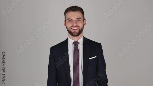 Young handsome businessman looking at camera, grey background, isolated, in suit and tie, looking tired