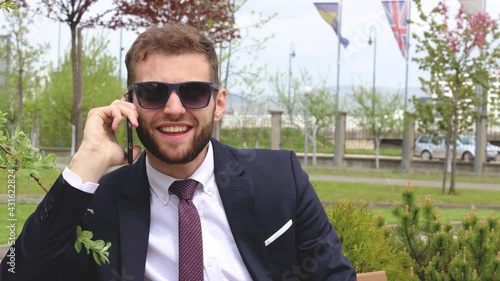 Young manager sitting on a bench, wearing black sunglasses, smiling and talking on phone