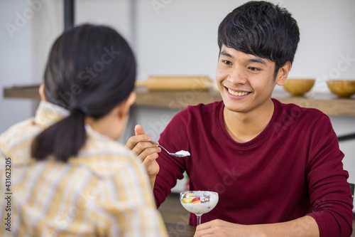Portrait shot of cute smiling handsome young adult husband eating ice cream at a dessert cafe with a wife in the foreground. Young couple lovers eating ice cream together at restaurant with happiness