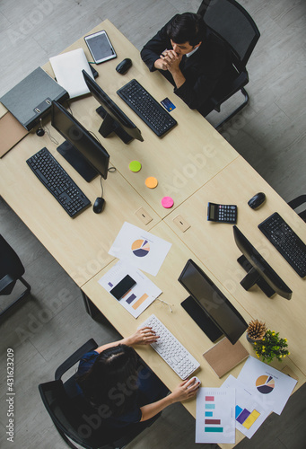 Top view portrait shot of a male and female professional Asian business employee sitting at wooden table and working by using a computer at the office. Concept of business workplace, company workers