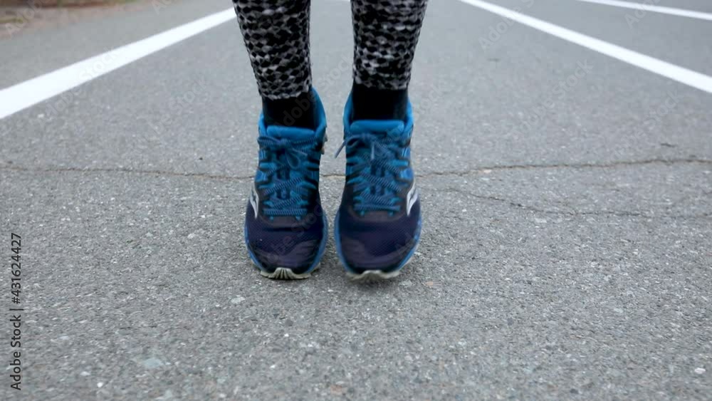 Sports running. Close-up. The athlete shifts from foot to foot in sneakers on the asphalt road. Girl athlete runs on the spot. Sports running. Close-up. The athlete shifts from foot to foot in sneakers on the asphalt road. Girl athlete runs on the spot.
