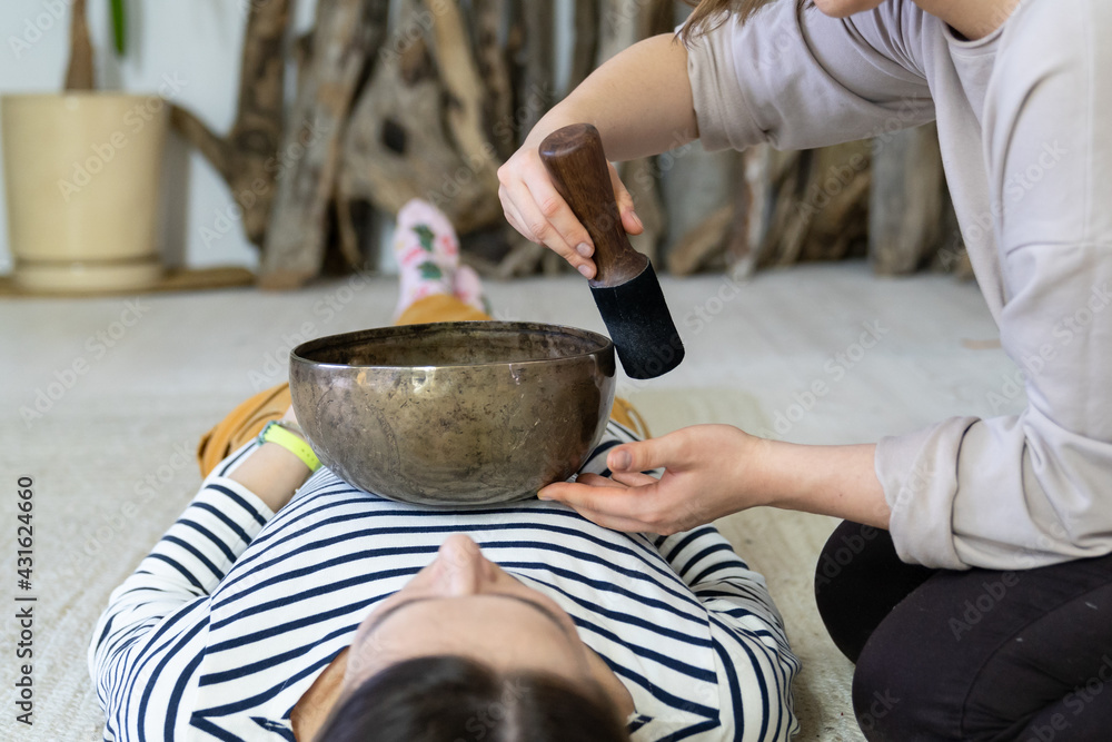 Young female having tibetan massage, singing bowl therapy with traditional tibet cymbals at home. Caucasian woman relax with alternative buddhism medicine. Wellbeing, wellness, stress relief concept Young female having tibetan massage, singing bowl therapy with traditional tibet cymbals at home. Caucasian woman relax with alternative buddhism medicine. Wellbeing, wellness, stress relief concept