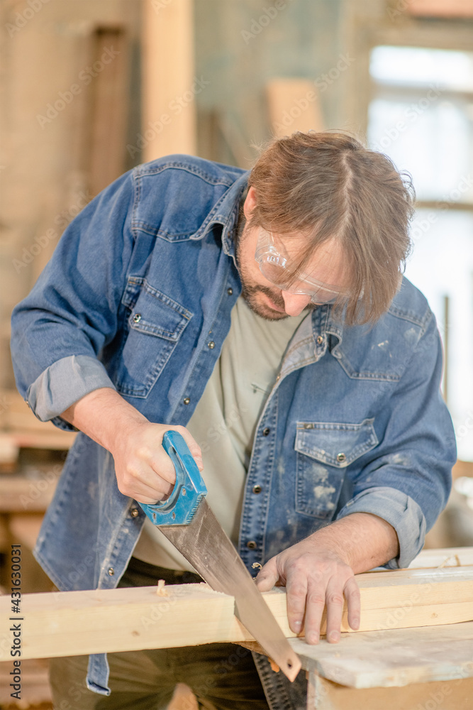 Carpenter sawing a board with a hand wood saw in carpentry workshop