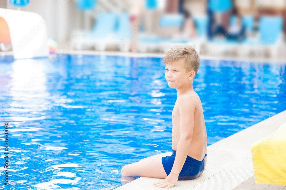 Young boy sits near a pool. Empty space for text