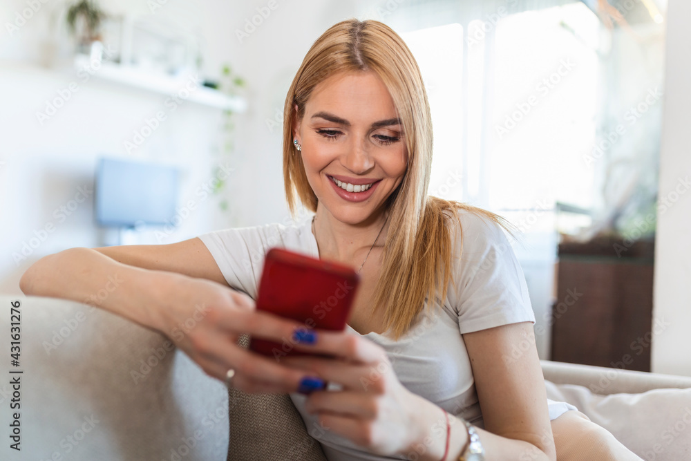 Attractive smiling woman using smart phone while sitting on the sofa at home. Communication and coziness concept. Attractive smiling woman using smart phone while sitting on the sofa at home. Communication and coziness concept.