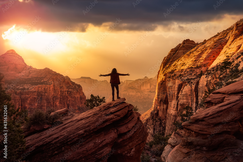 Adventurous Woman at the edge of a cliff is looking at a beautiful landscape view in the Canyon. Sunset Sky Art Render. Taken in Zion National Park, Utah, United States.