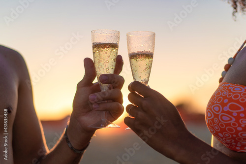 Closeup cut on hands clinking with champagne on the beach at sunset. Dating concept, backlight.