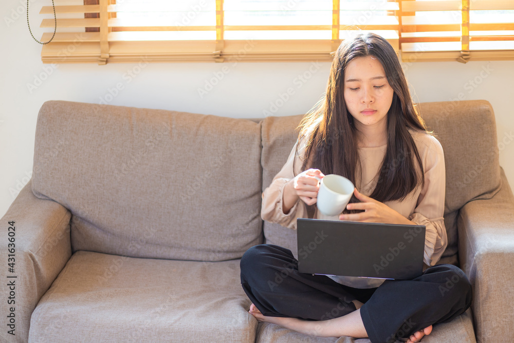Woman sitting on sofa in an apartment drink coffee and opened laptop working at home Woman sitting on sofa in an apartment drink coffee and opened laptop working at home