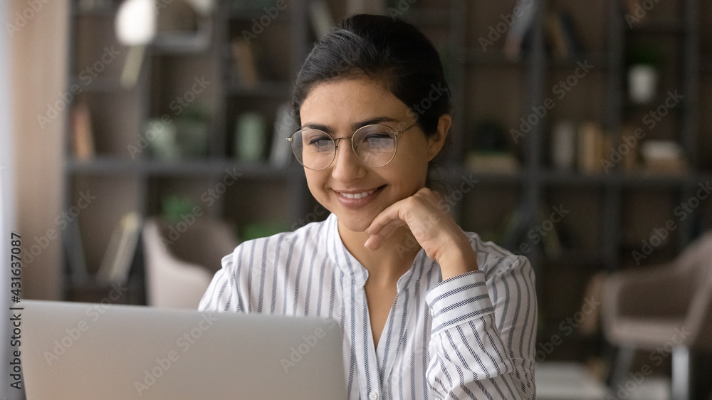 Close up smiling Indian businesswoman in glasses looking at laptop screen, working on project, reading good news in email, positive young woman using computer, student studying online at home office Close up smiling Indian businesswoman in glasses looking at laptop screen, working on project, reading good news in email, positive young woman using computer, student studying online at home office