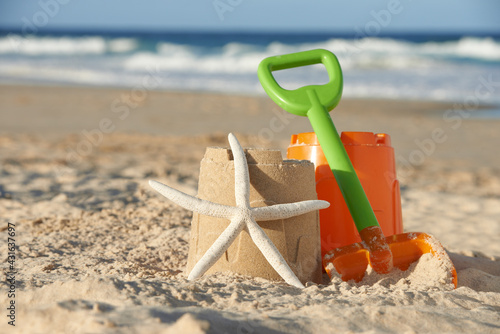 Bucket and spade next to starfish leanding against sandcastle at the beach photo