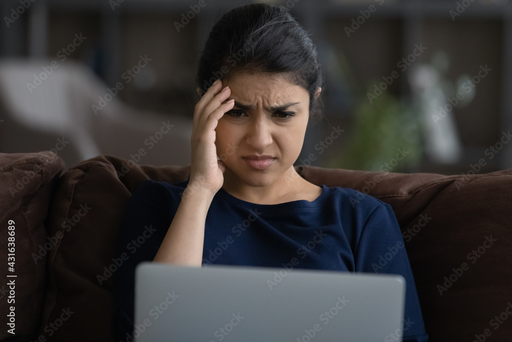 Close up unhappy Indian woman looking at laptop screen, reading bad news in message or social network, sitting on couch at home, worried businesswoman freelancer received dismissal notification Close up unhappy Indian woman looking at laptop screen, reading bad news in message or social network, sitting on couch at home, worried businesswoman freelancer received dismissal notification