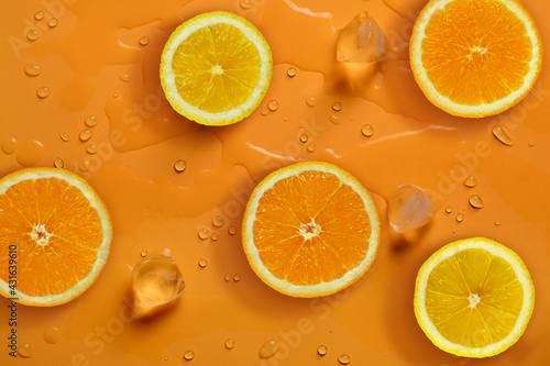 Fresh juicy slices of orange and lemon on bright orange background covered with water drops. Creative food background, top view