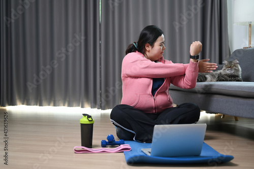 Obese woman stretching arms before exercises at home.