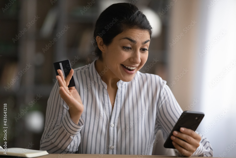 Close up excited Indian woman holding credit card, using smartphone, reading good news, checking balance, surprised customer received money refund or great shopping offer, making internet payment