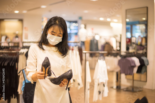 Young Asian woman wearing protective mask while choosing clothes in the store.concept of virus protection in the fashion, beauty, and shopping industries.concept of virus protection in the fashion, be