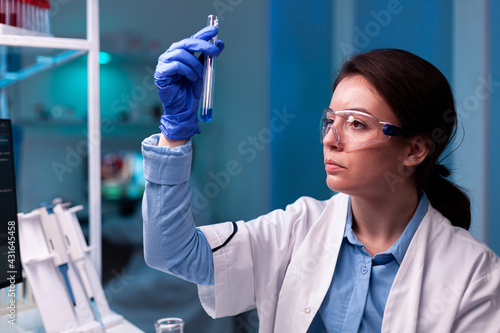 Scientist looking at testube with sample, analyzing liquid experiment. Pharmaceutical biotechnologist in research laboratory works with test tube to find vaccine glove. photo