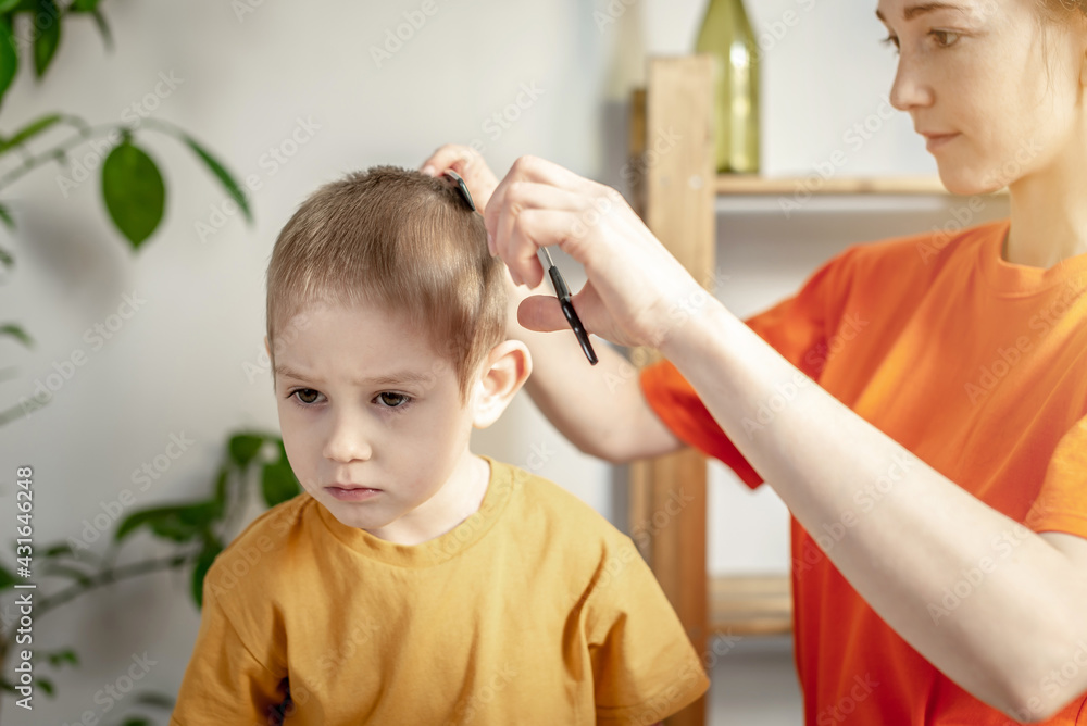 A young woman in bright clothes is cutting a little boy's hair with scissors. Concept of family, care, lifestyle A young woman in bright clothes is cutting a little boy's hair with scissors. Concept of family, care, lifestyle