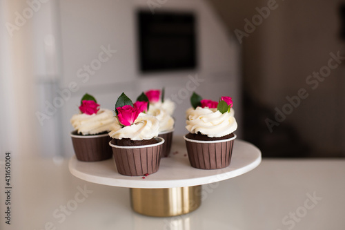 Cupcakes with cream cheese decorated with rose flowers stay on mable tray on kitchen table close up. Tasty homemade dessert.