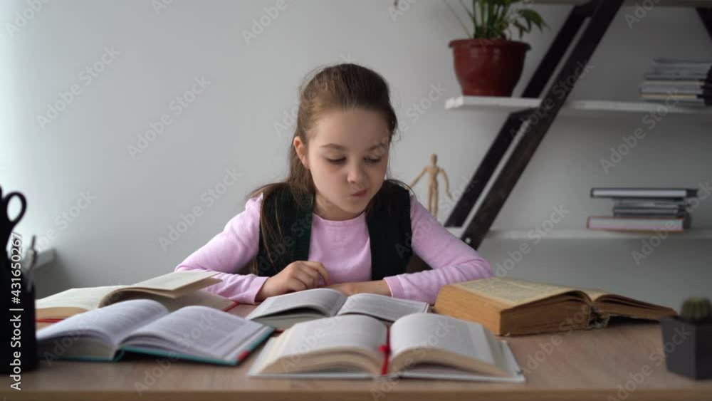 Young Caucasian girl is sitting at the table at home. Many open books. Search for the information you need. Exam preparation. Distance education concept. Young Caucasian girl is sitting at the table at home. Many open books. Search for the information you need. Exam preparation. Distance education concept.
