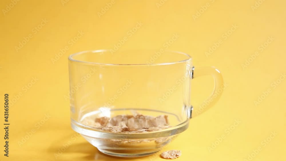 Transparent bowl with corn and multigrain flakes on a yellow background. The flakes fall into the cup. Quick and healthy breakfast Transparent bowl with corn and multigrain flakes on a yellow background. The flakes fall into the cup. Quick and healthy breakfast