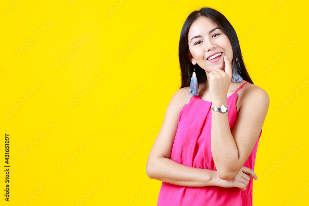 Asian beautiful cheerful adult woman with long black hair wearing pink dress, fashionable earring, wrist watch, happily smiling, putting hand on chin with isolated yellow background and copy space. Asian beautiful cheerful adult woman with long black hair wearing pink dress, fashionable earring, wrist watch, happily smiling, putting hand on chin with isolated yellow background and copy space.