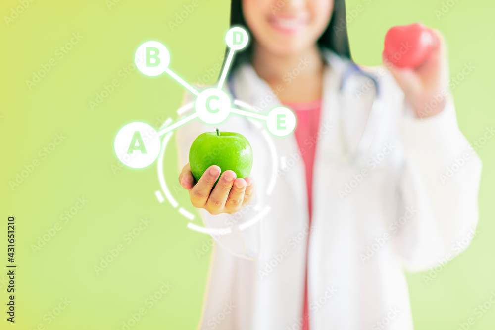 Selective focus and close up to hand holding green apple with mixed vitamin icons. Blur female nutrition doctor on isolated light green background. Healthy and Vitality Concept. Selective focus and close up to hand holding green apple with mixed vitamin icons. Blur female nutrition doctor on isolated light green background. Healthy and Vitality Concept.