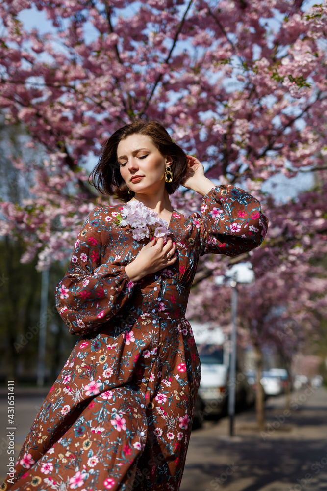 Portrait of a cute and beautiful woman girl in a dress in the garden in the middle of blooming sakura. spring and sun time. Blurred background and selected focus. Portrait of a cute and beautiful woman girl in a dress in the garden in the middle of blooming sakura. spring and sun time. Blurred background and selected focus.