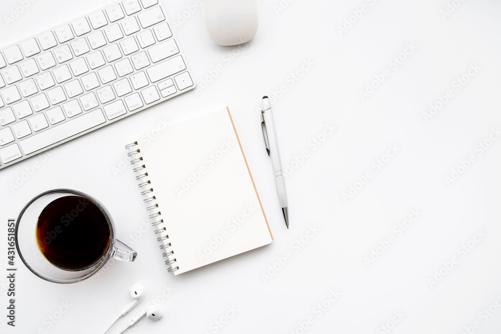 Blank notebook is on top of white office desk table with cup of coffee and computer supplies. Top view with copy space, flat lay. Blank notebook is on top of white office desk table with cup of coffee and computer supplies. Top view with copy space, flat lay.