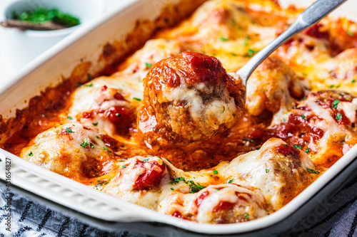 Closeup of baked cheesy meatballs casserole with tomato sauce in the oven dish.