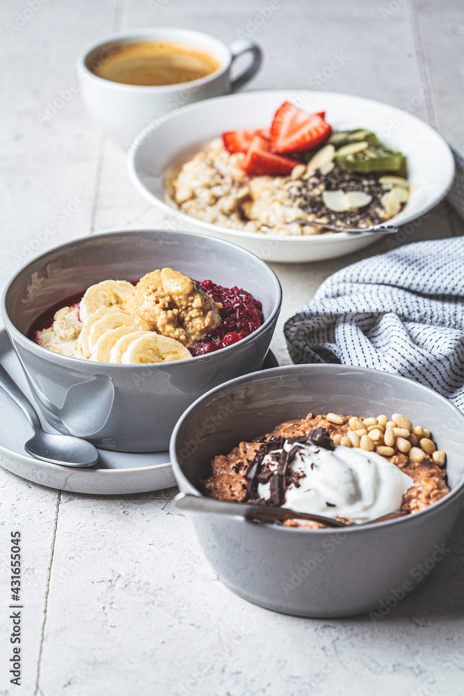 Assorted oatmeal bowls with chocolate, fruit, berry, yogurt and coffee, gray tiles background. Healthy breakfast concept. Assorted oatmeal bowls with chocolate, fruit, berry, yogurt and coffee, gray tiles background. Healthy breakfast concept.