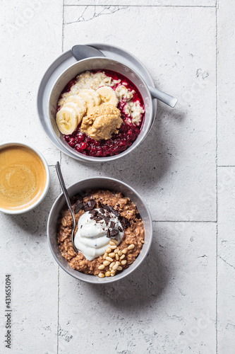 Oatmeal bowls with chocolate, yogurt, fruit and peanut butter, gray tiles background. Healthy breakfast concept.