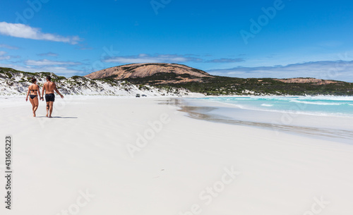 A young couple stoll along on the prisitine white sand beach and sparkling waters of Wharton Bay in the Cape LeGrande National Park on a clear summer day.