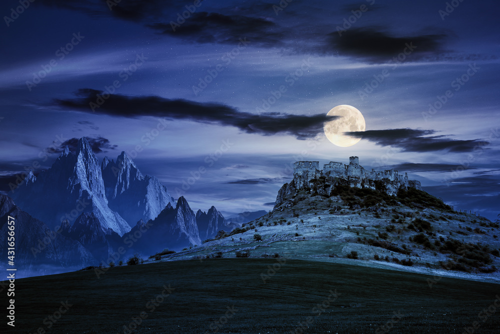 Obraz premium castle on the hill at night. composite fantasy landscape. grassy meadow in the foreground. rocky peaks of the ridge in the distant background in full moon light