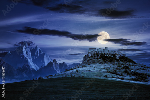 castle on the hill at night. composite fantasy landscape. grassy meadow in the foreground. rocky peaks of the ridge in the distant background in full moon light