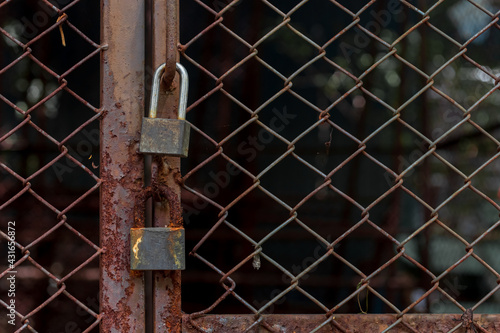Abandoned padlocks locked on rusty wire mesh steel door background.