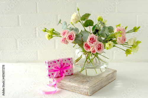 bouquet of Roses, eustoma and eucalyptus in a glass stylish vase on a table next to the love gift. Flowers composition for interior decoration.