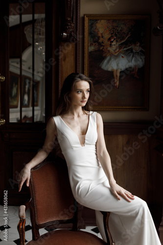 A stylish modern bride in a white dress with a cutout, a conceptual image. A trendy image of the bride in a dark interior, laconic European style.