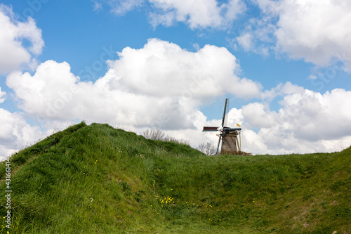 Dutch windmill on top of a lush green field in the Netherlands, cloudy sky background  photo