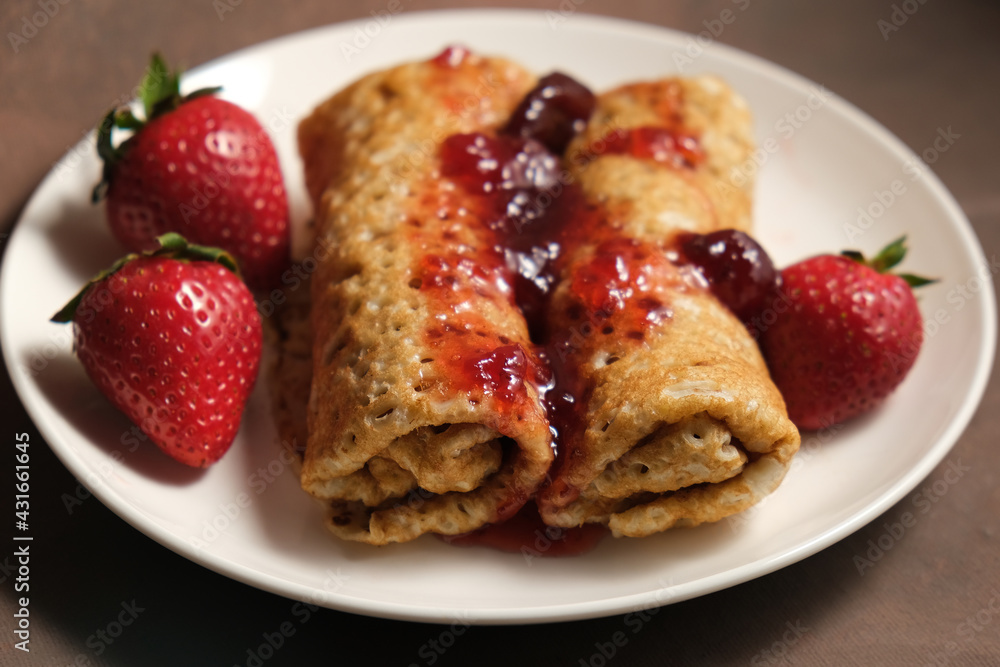Pancakes with strawberry jam on plate. Pancakes rolls poured berry jam and decorated fresh strawberries. Pancakes with strawberry jam on plate. Pancakes rolls poured berry jam and decorated fresh strawberries.
