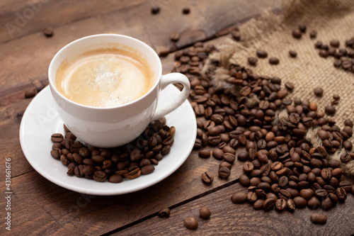 Cup of freshly brewed coffee on wooden table with roasted coffee beans on wooden background