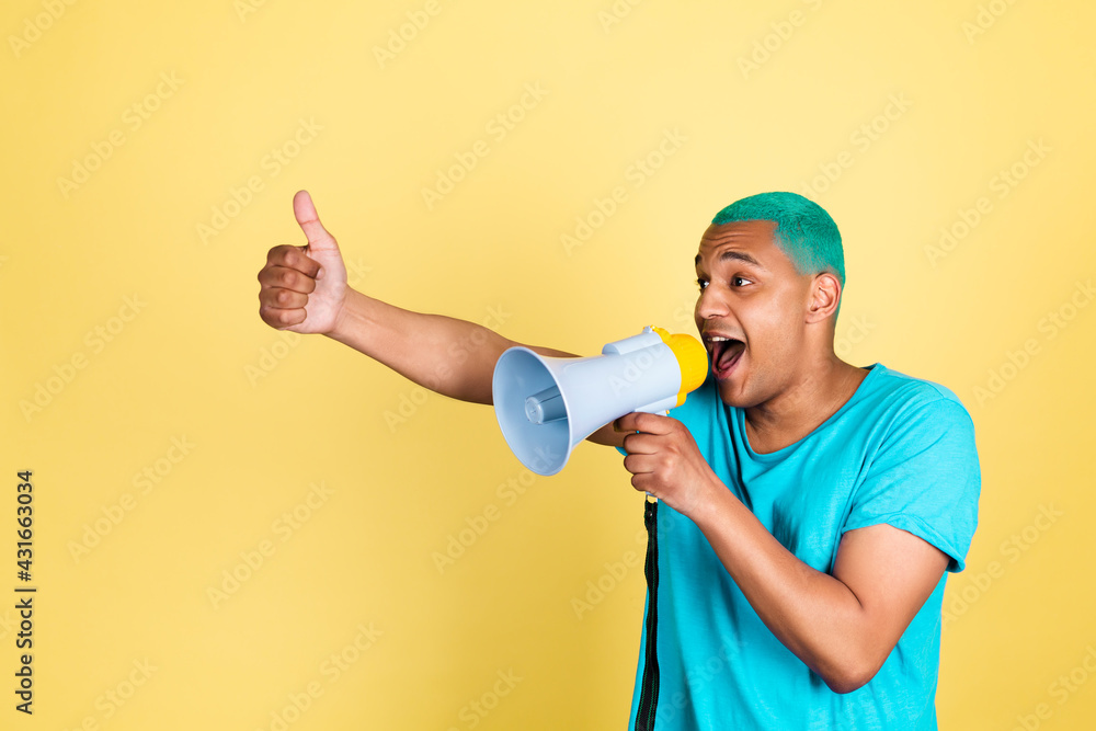 Black african man in casual on yellow background blue hair screaming shouting in megaphone to left show thumb up Black african man in casual on yellow background blue hair screaming shouting in megaphone to left show thumb up