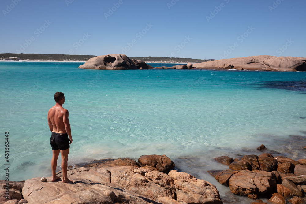 Landscape view of an athletic young man viewing the pristine white sands, crystal clear aqua water and granite boulders on a clear blue day at Twilight Cove, near Esperance in Western Australia.