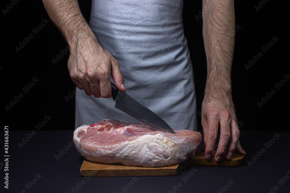 Pork meat on a black background. The cook cuts a piece of meat on a dark background. Raw pork leg. Fresh raw meat.