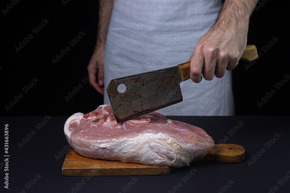 Pork meat on a black background. The cook cuts a piece of meat on a dark background. Raw pork leg. Fresh raw meat.
